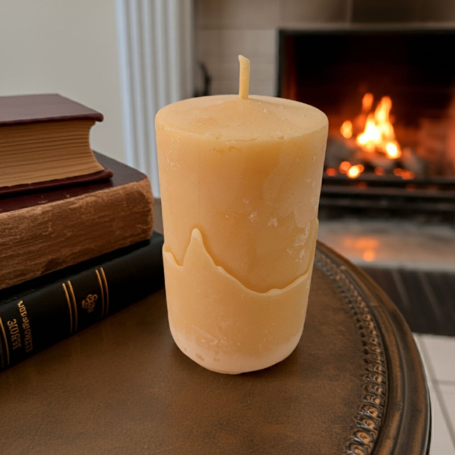 Smooth Pillar Beeswax Candle on a table with books and a fireplace in the background