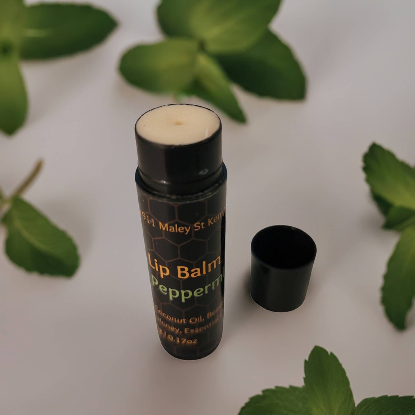 Lip balm with peppermint flavor on a white background with mint leaves.
