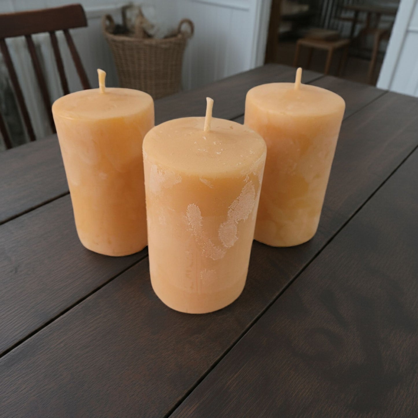 Three 2x3 smooth pillar beeswax candles on a country style wooden table.