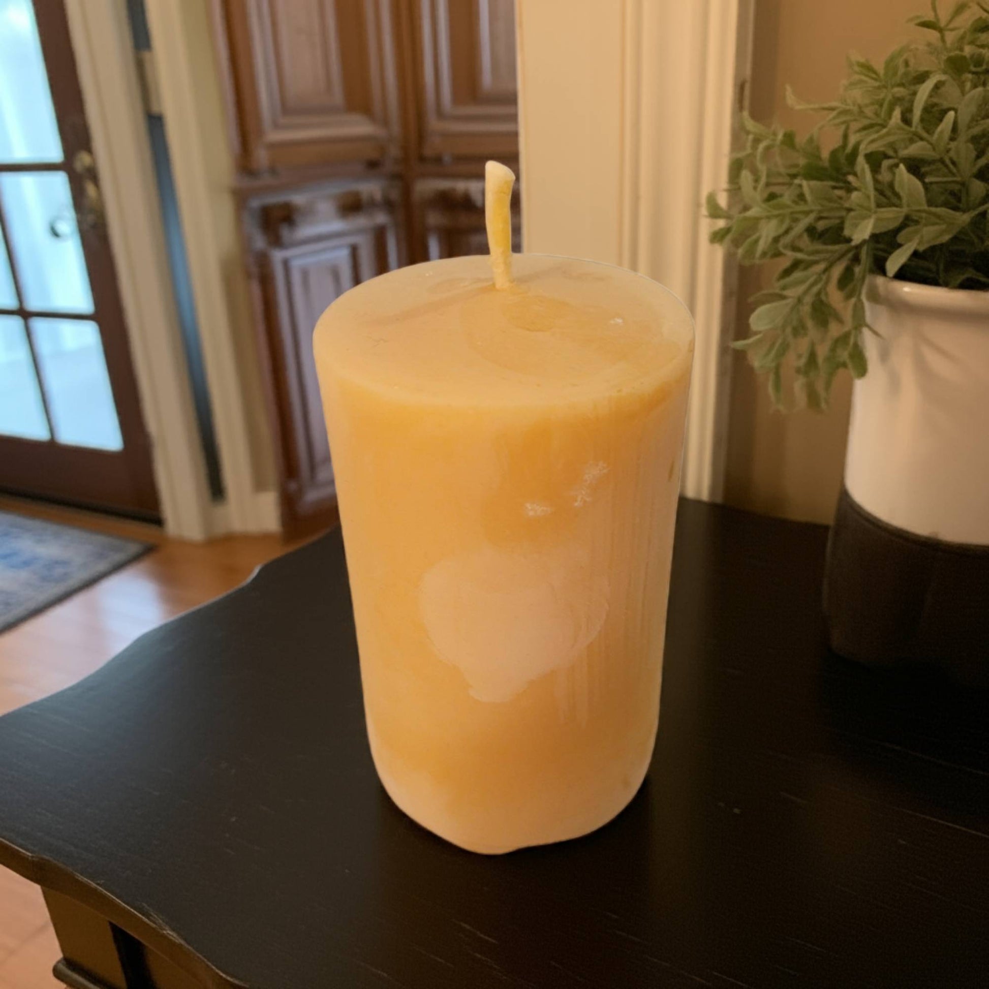 Beeswax candle in a glass jar on a dark surface with a plant in the background