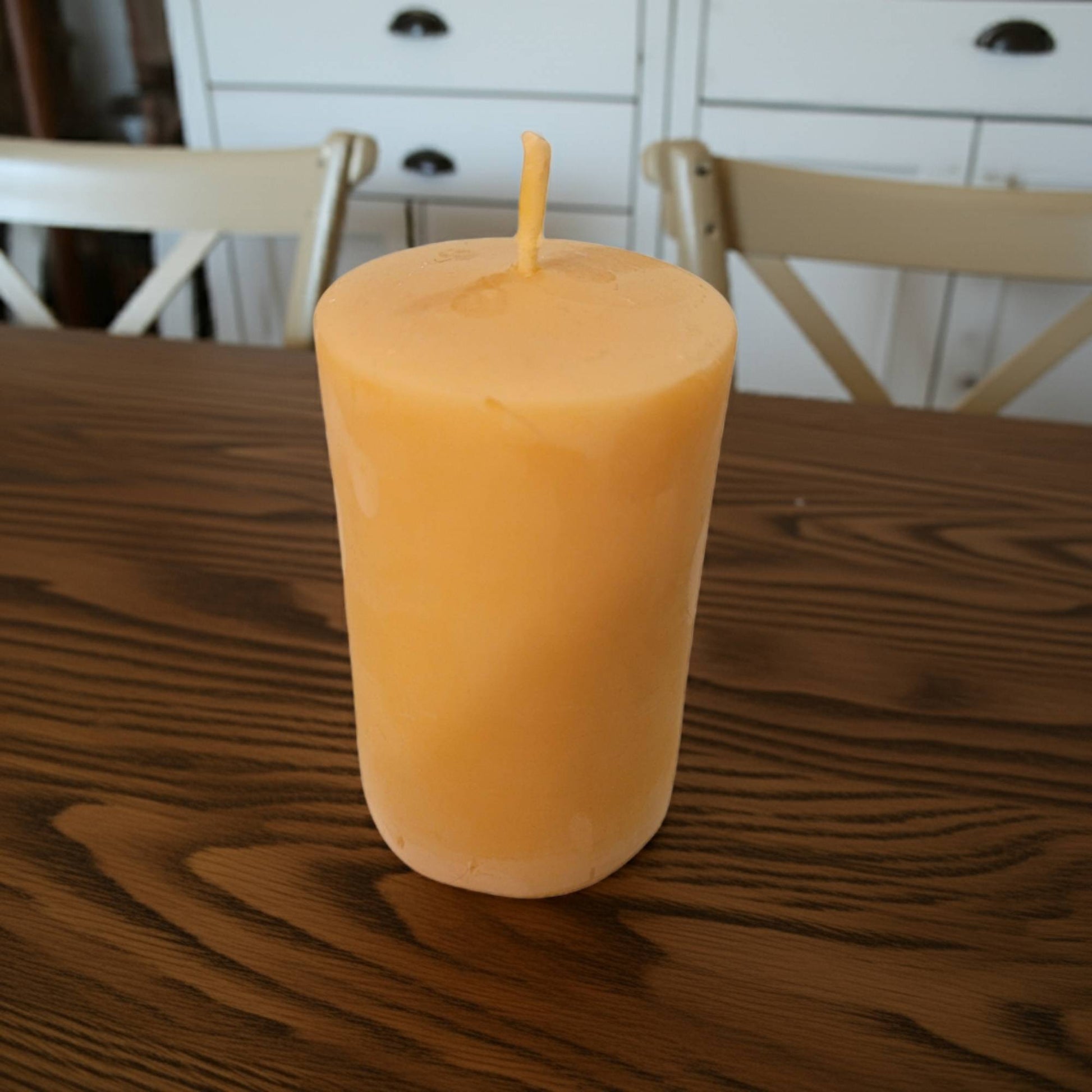 2x3 smooth pillar beeswax candle on a wooden table with white chairs in the background
