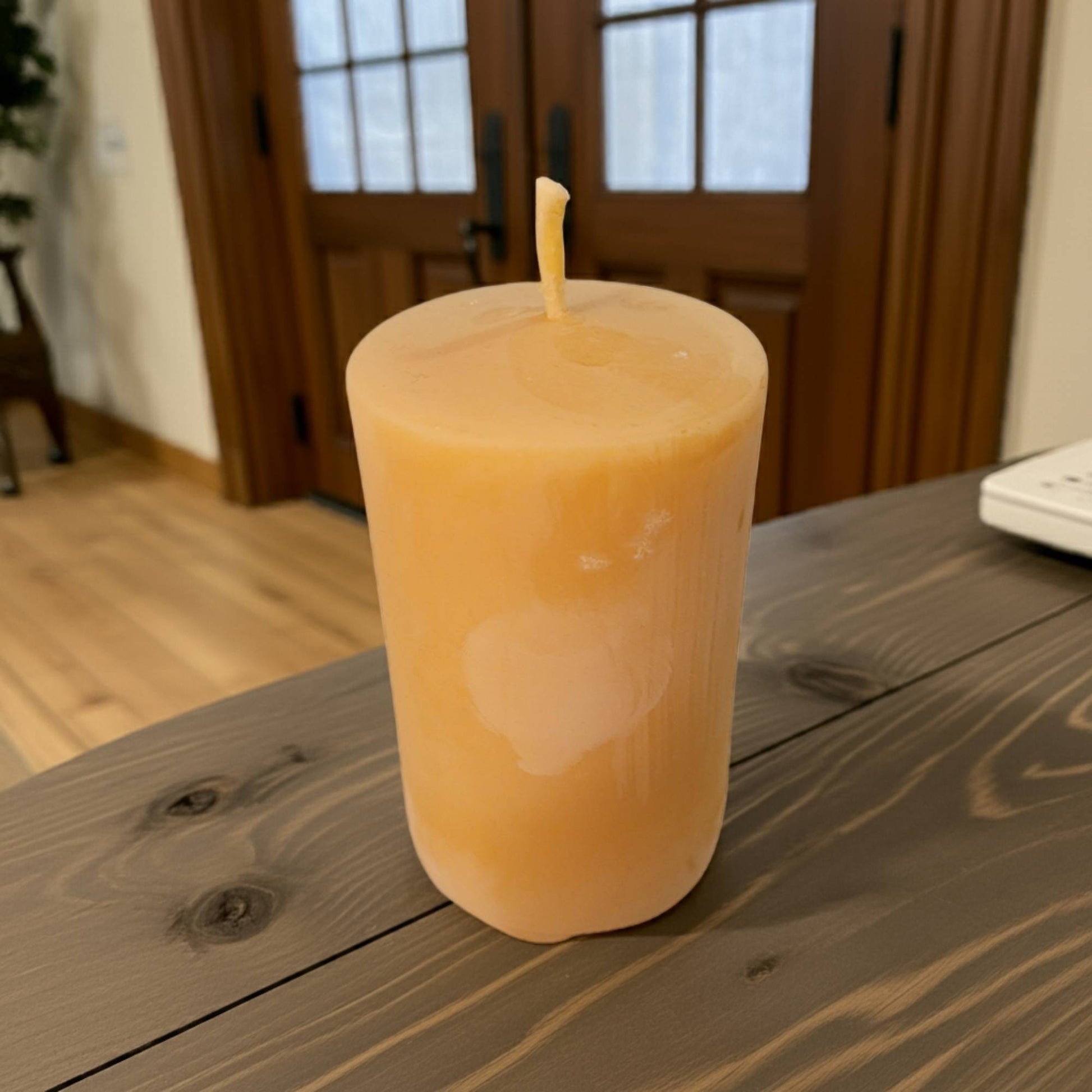 2x3 smooth pillar beeswax candle on a wooden table with a blurred background