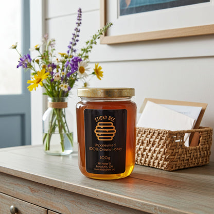 Jar of Sticky Bee honey on a wooden surface with flowers and a basket in the background