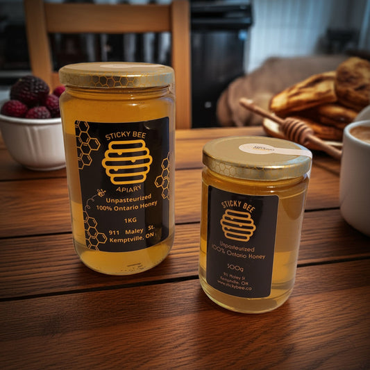 Two jars of Sticky Bee Apiary honey on a wooden table with a blurred background.