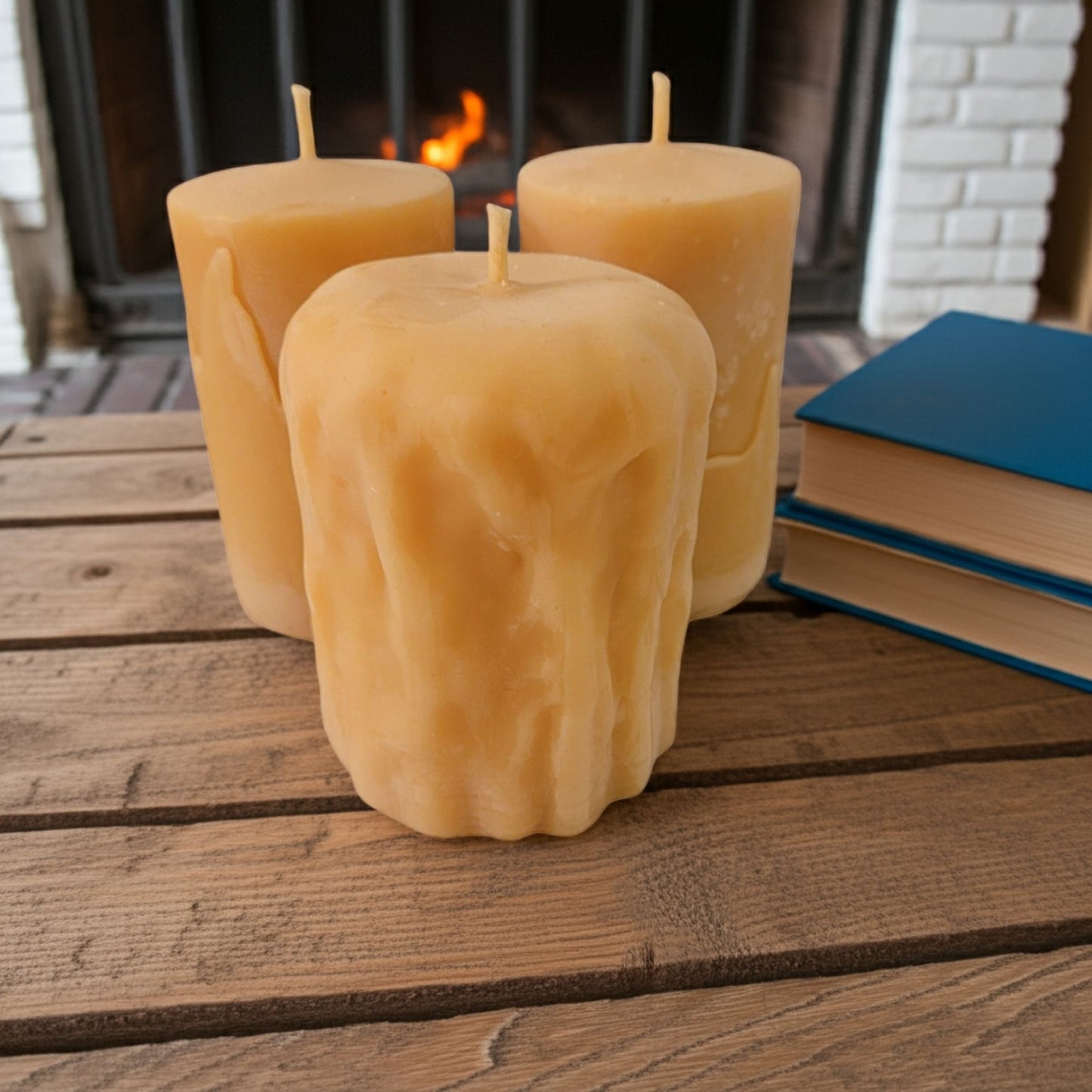 Three textured candles on a wooden surface with a fireplace in the background
