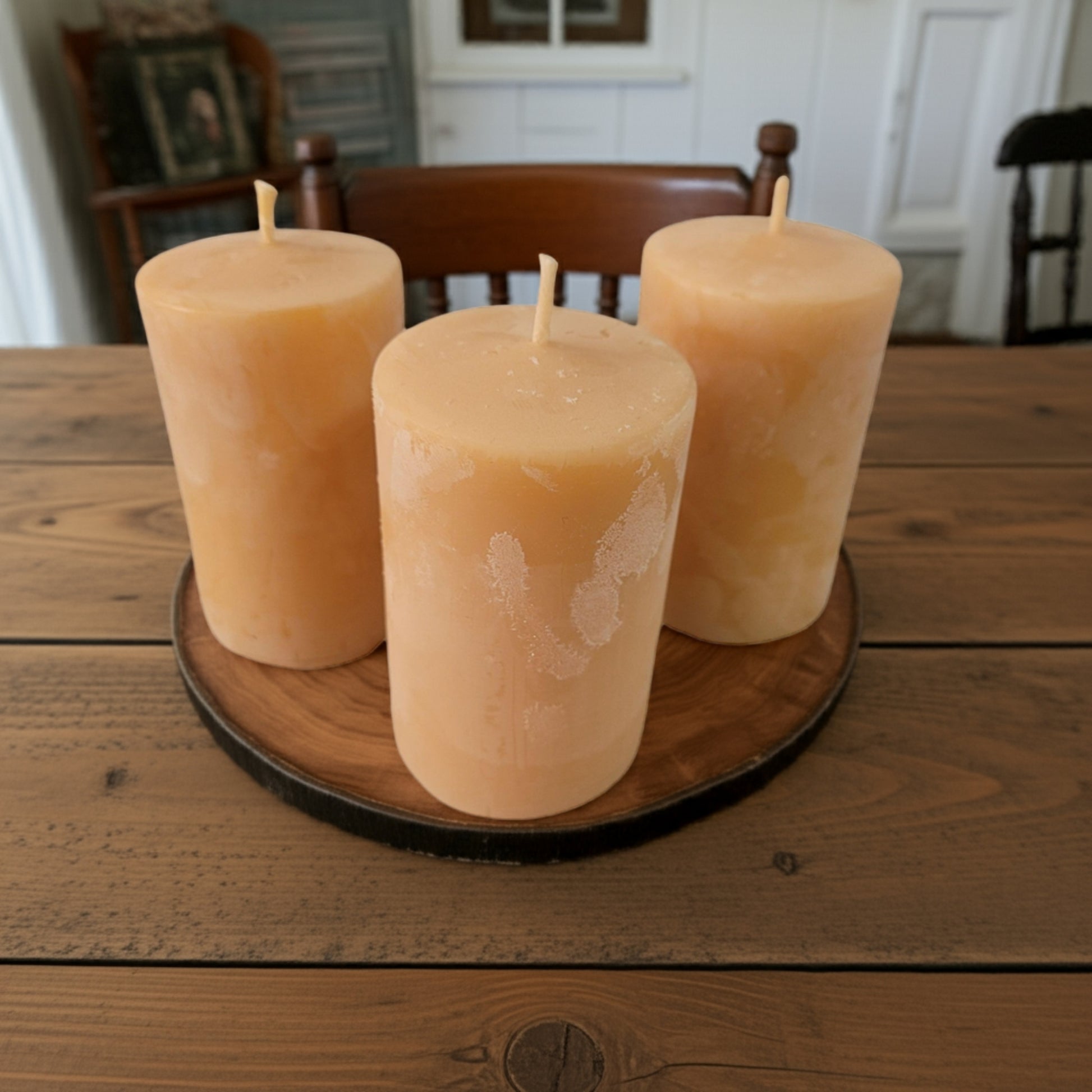 Three 2x3 smooth pillar beeswax candles on a wooden tray on a rustic wooden table