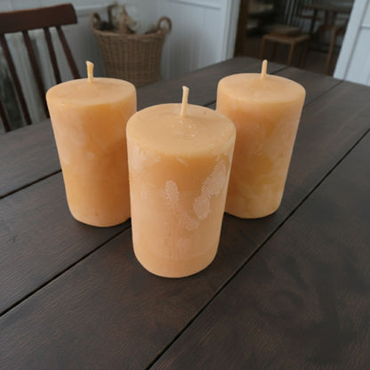 Three 2x3 smooth pillar beeswax candles on a country style wooden table.