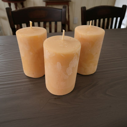 Three 2x3 smooth pillar beeswax candles on a rustic wooden table.