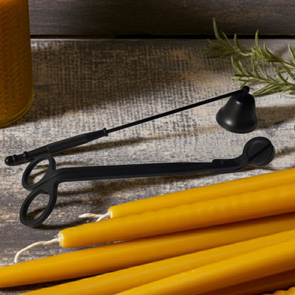 Black candle snuffer and yellow candles on a textured surface with a plant in the background