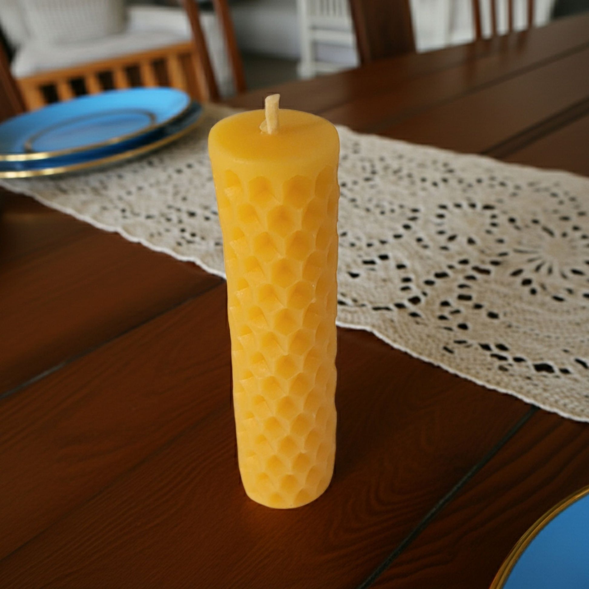 Yellow honeycomb-patterned candle on a wooden table with a doily underneath
