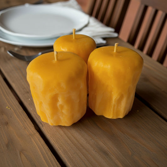 Three yellow candles on a wooden table with a plate and cutlery in the background.