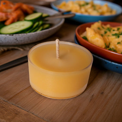 Yellow candle on a wooden surface with food items in the background