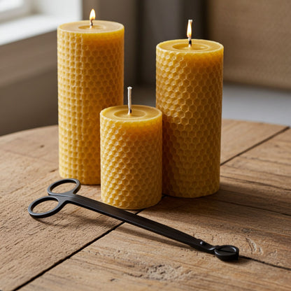 Three honeycomb-patterned beeswax candles on a wooden surface with a pair of black wick trimmers.
