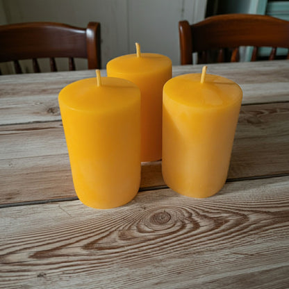 Three yellow candles on a wooden table with chairs in the background