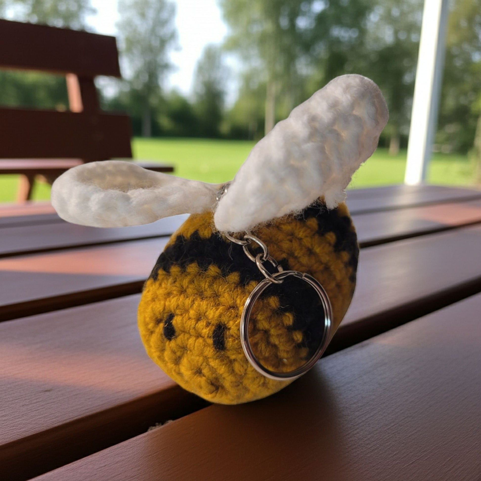 Yellow bee-shaped keychain with black spots on a wooden surface outdoors