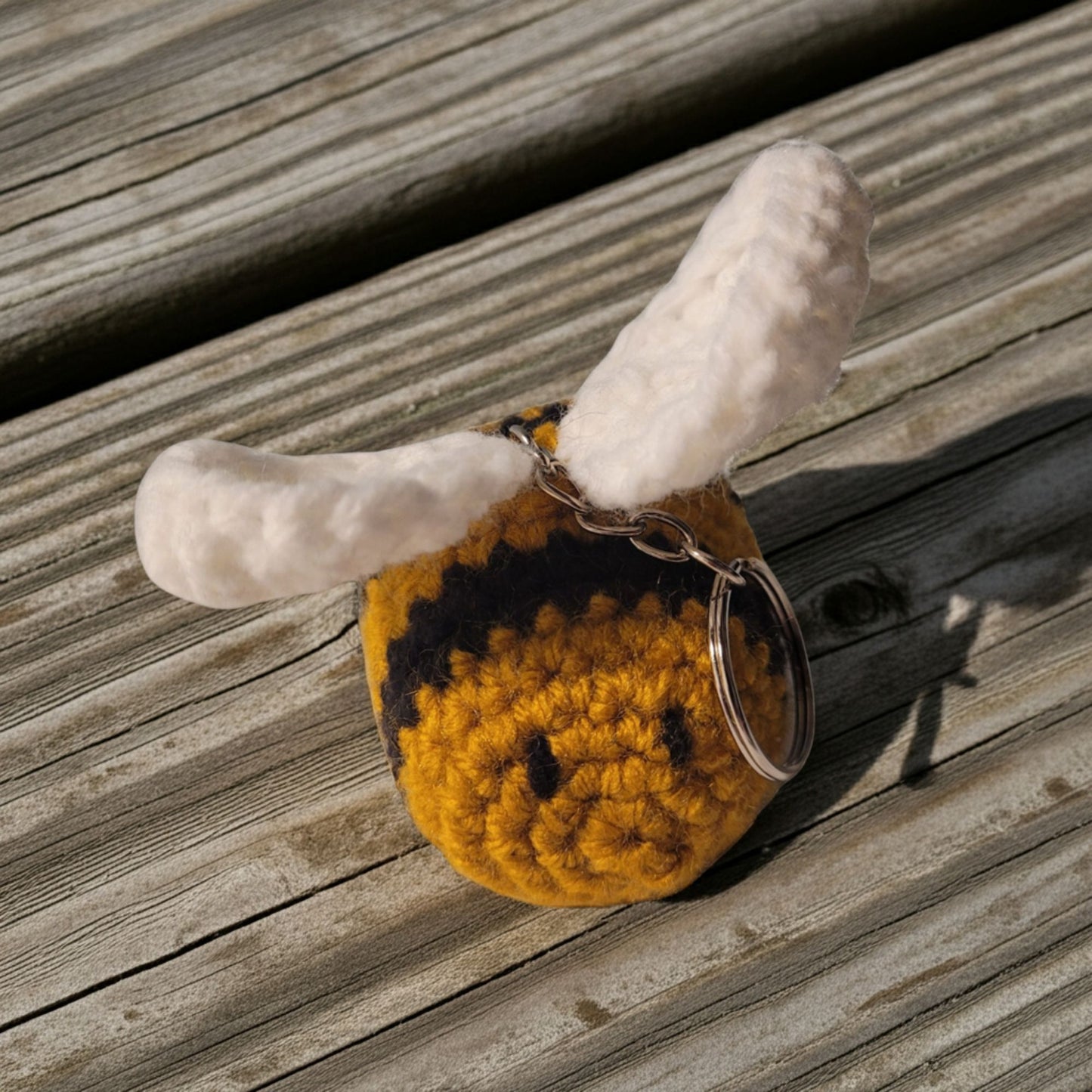 Crocheted bee keychain with white wings on a wooden surface