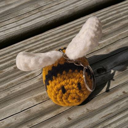 Crocheted bee keychain with white wings on a wooden surface
