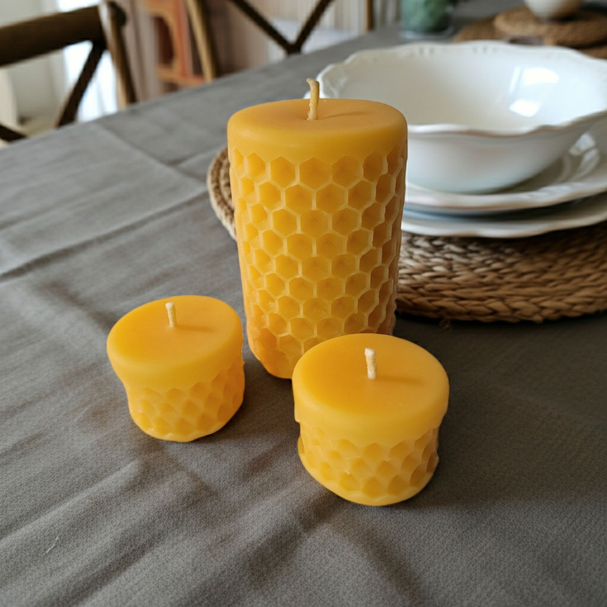 Three yellow beeswax candles with honeycomb pattern on a gray tablecloth.