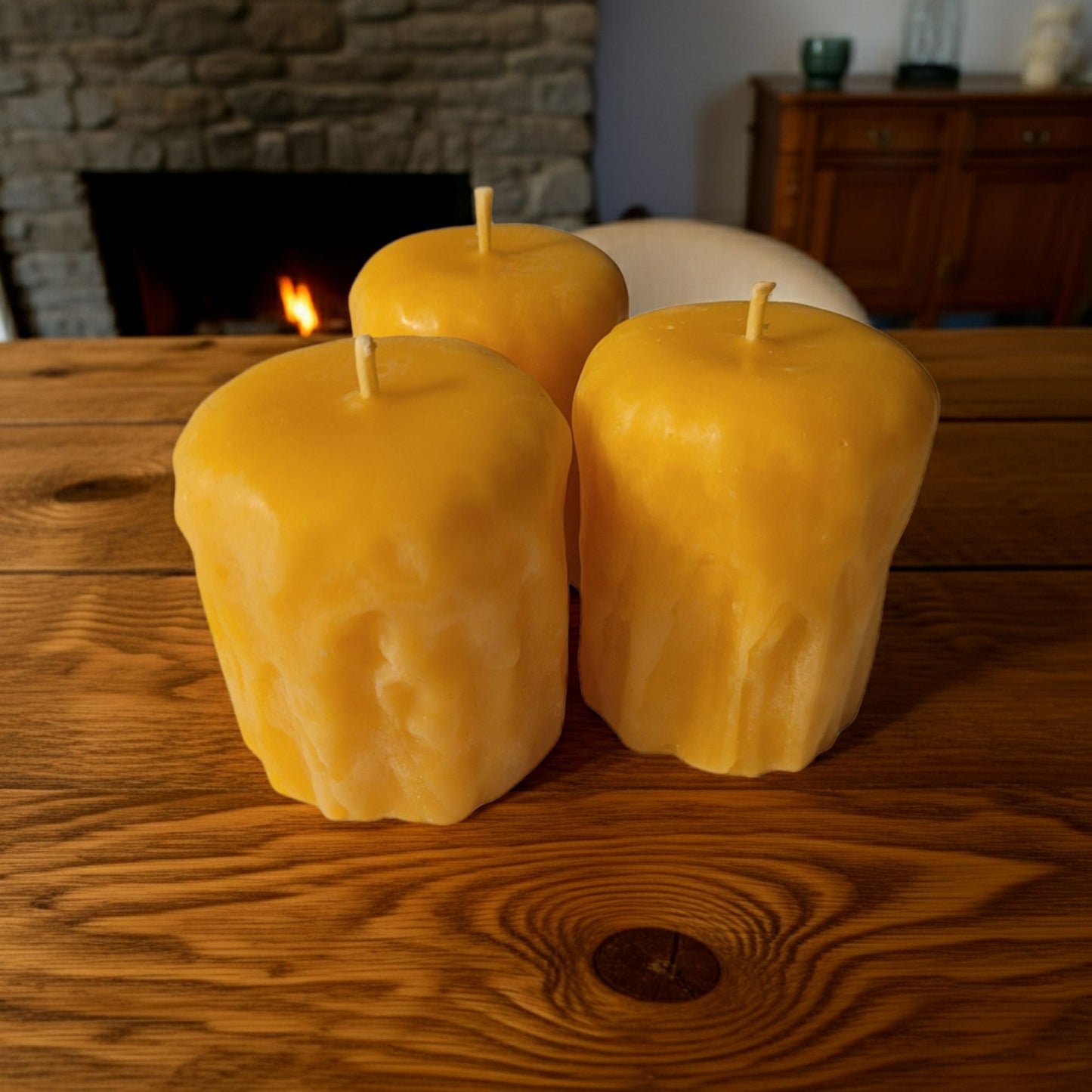 Three yellow candles on a wooden surface with a fireplace in the background