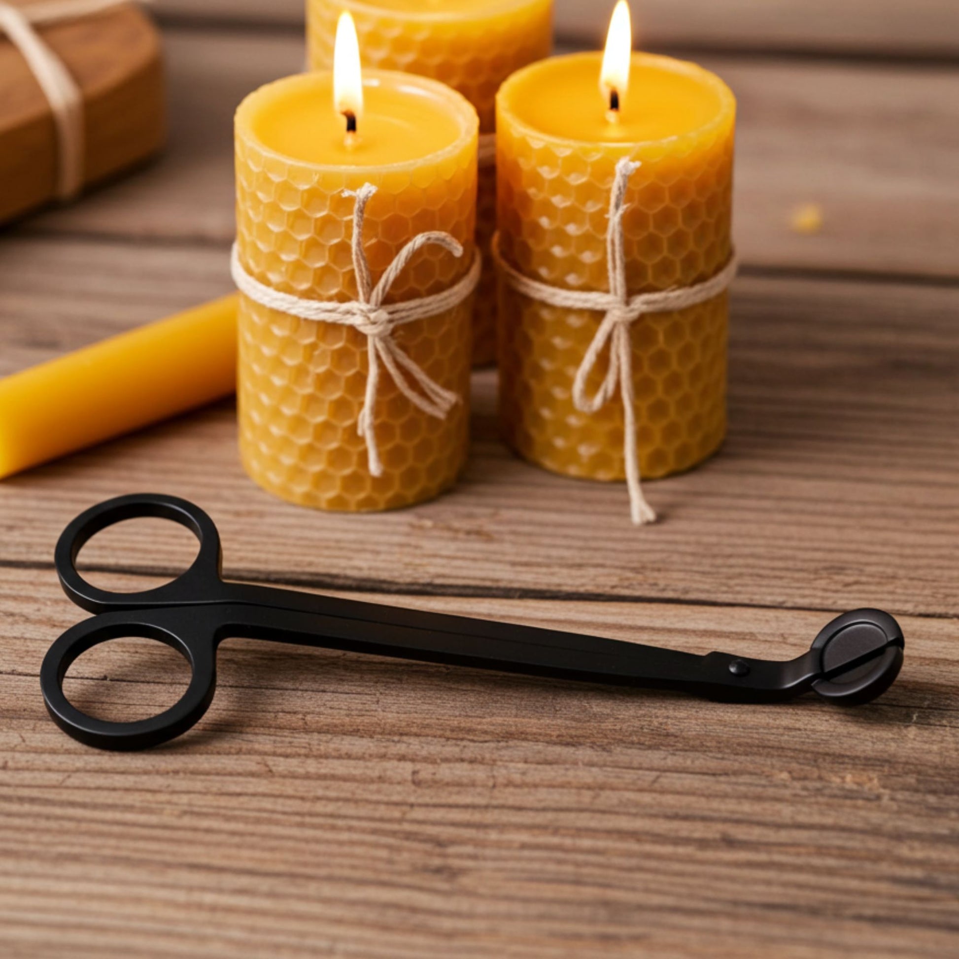 Three lit beeswax candles with honeycomb texture on a wooden surface, accompanied by a pair of black candle scissors.