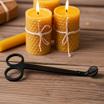 Three lit beeswax candles with honeycomb texture on a wooden surface, accompanied by a pair of black candle scissors.