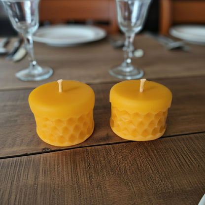 Two yellow candles with a honeycomb pattern on a wooden table.