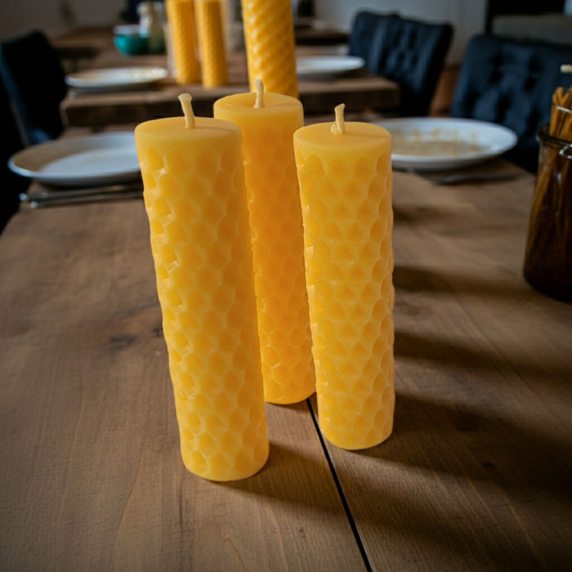 Three pure beeswax candles on a wooden table with a blurred background of a dining area.