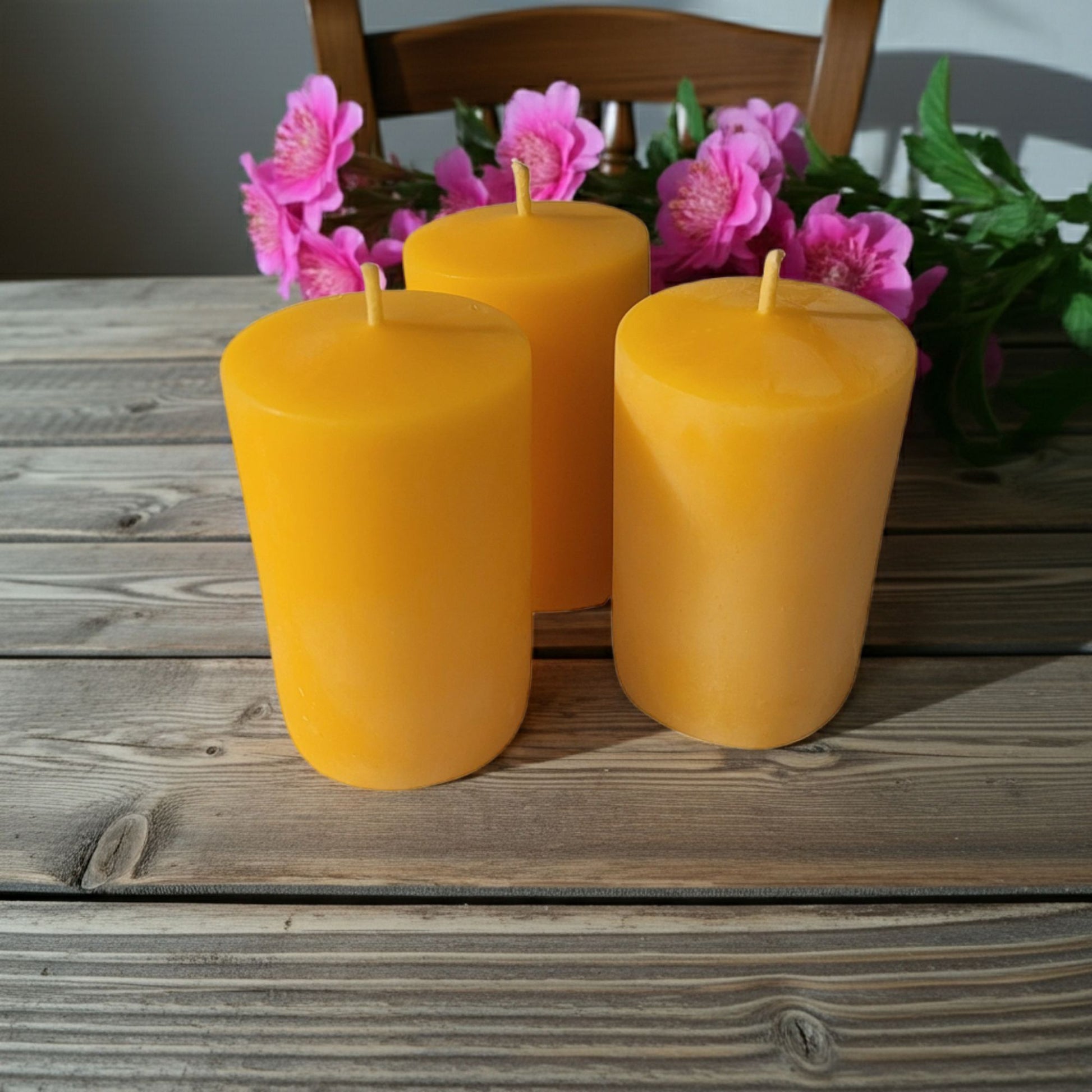 Three yellow candles on a wooden table with pink flowers in the background