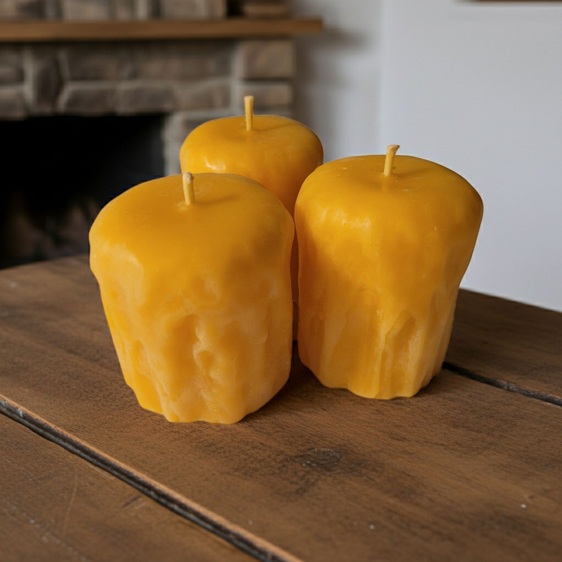 Three yellow candles on a wooden surface with a fireplace in the background
