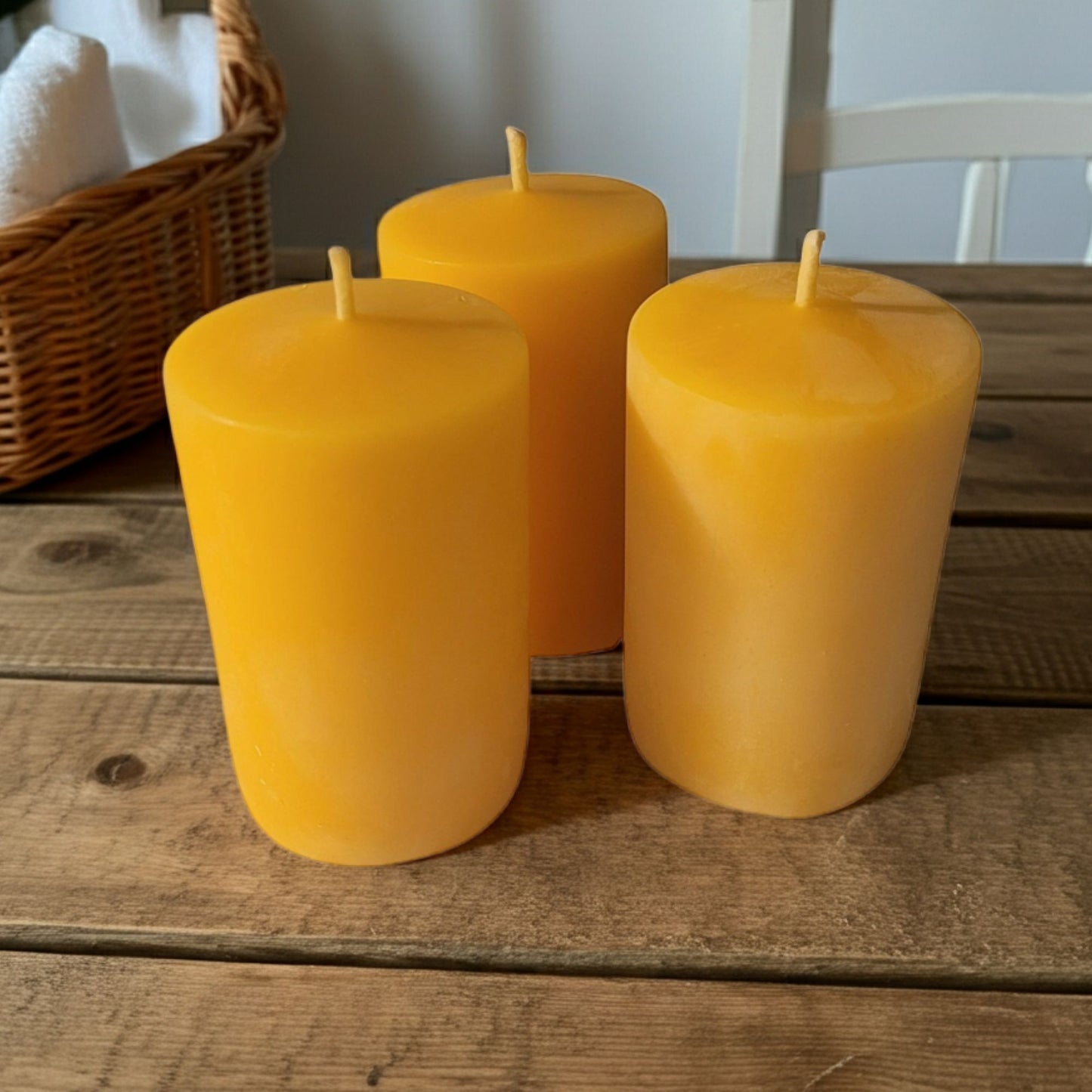 Three yellow candles on a wooden surface with a wicker basket in the background.