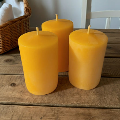 Three yellow candles on a wooden surface with a wicker basket in the background.