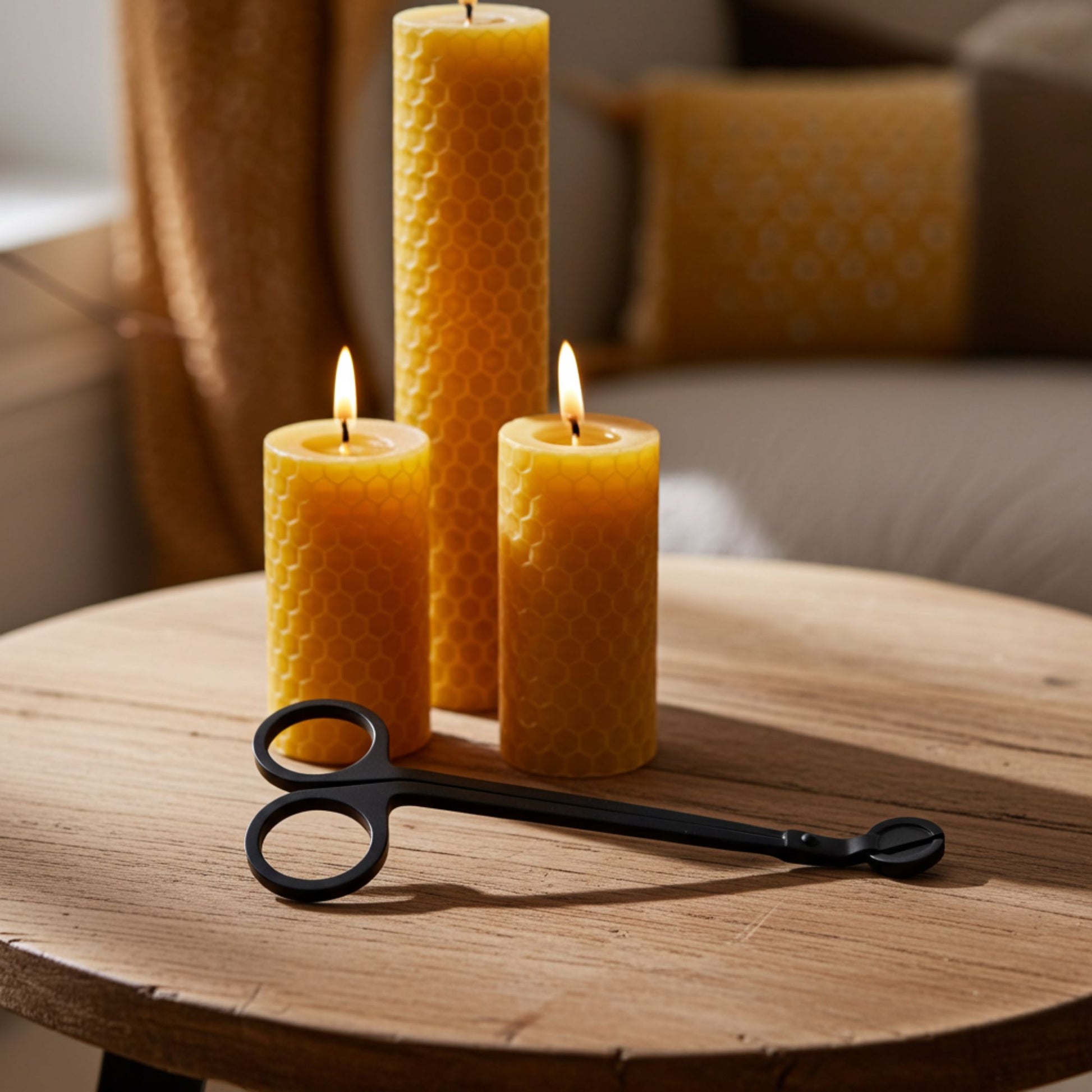 Three beeswax candles on a wooden table with a pair of wick trimmers.