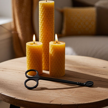 Three beeswax candles on a wooden table with a pair of wick trimmers.